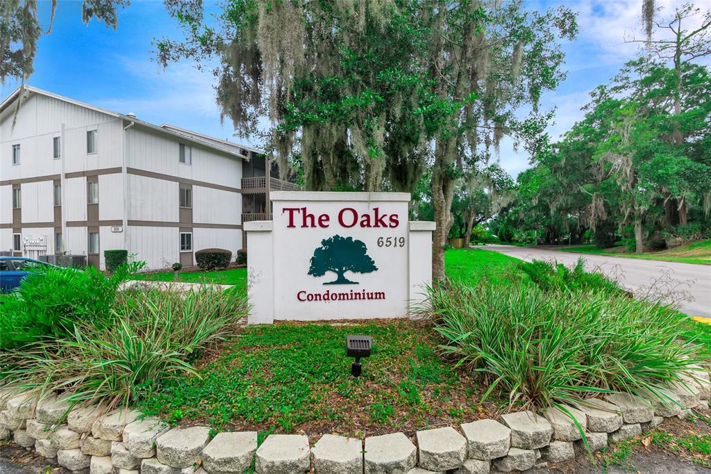 A sign for The Oaks Condominium stands in front of a multi-story residential building — 6519 W NEWBERRY ROAD UNIT A10, GAINESVILLE, FL