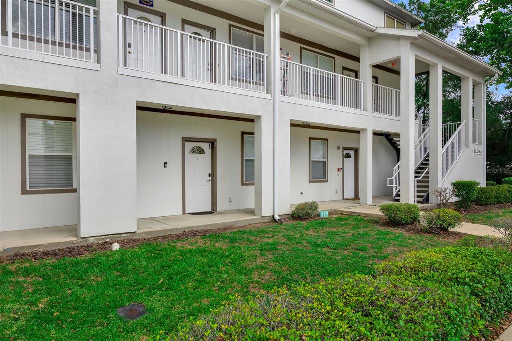 The exterior of a two-story apartment building features white stucco walls, balconies, and staircases — 6519 W NEWBERRY ROAD UNIT A10, GAINESVILLE, FL