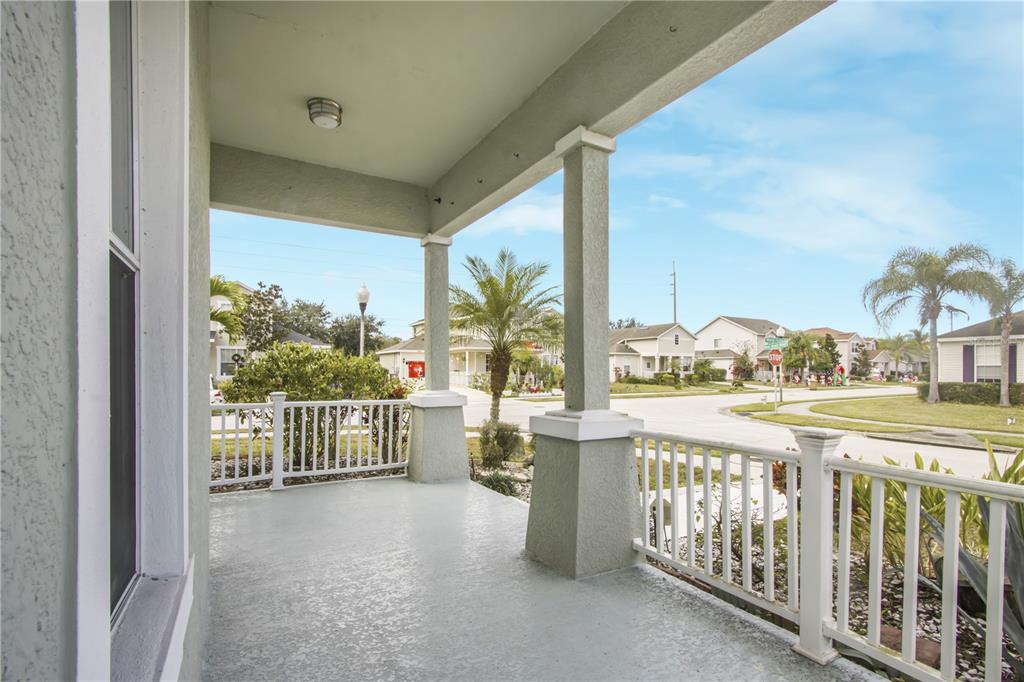 A covered front porch with a concrete floor, white railings, and two stucco support columns — 4988 BOND STREET W, KISSIMMEE, FL