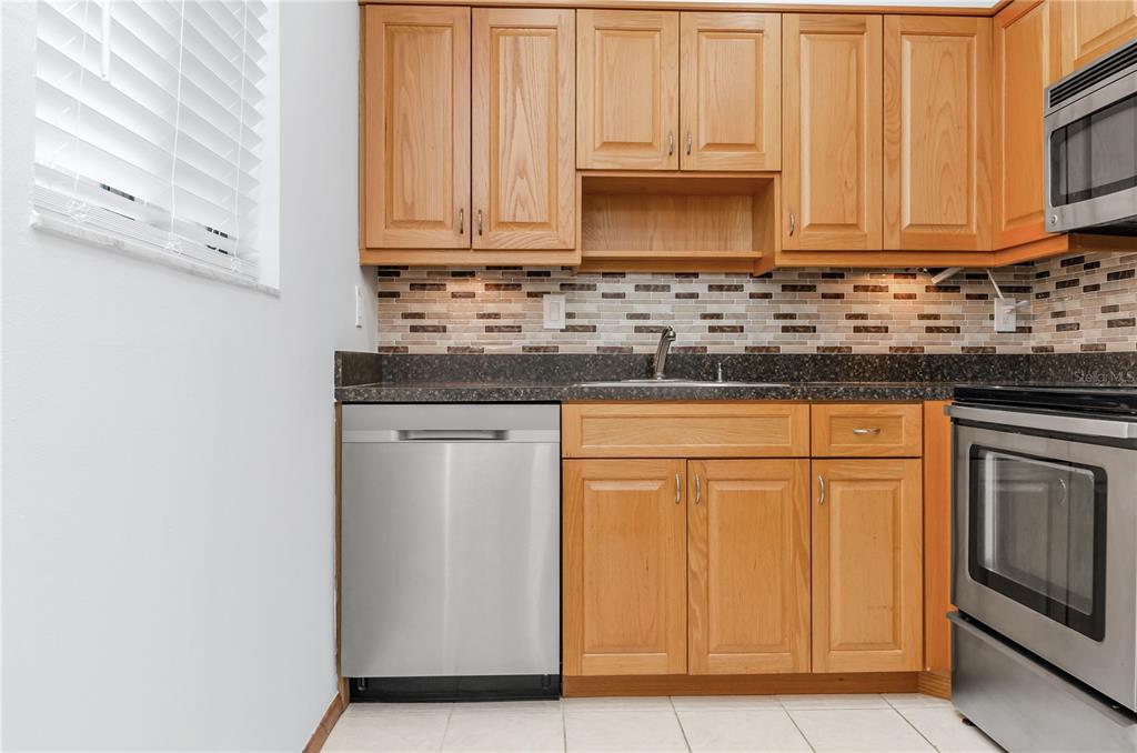 A kitchen features light wood cabinets, stainless steel appliances, and a mosaic tile backsplash — 3300 FOX CHASE CIRCLE N UNIT 231, PALM HARBOR, FL