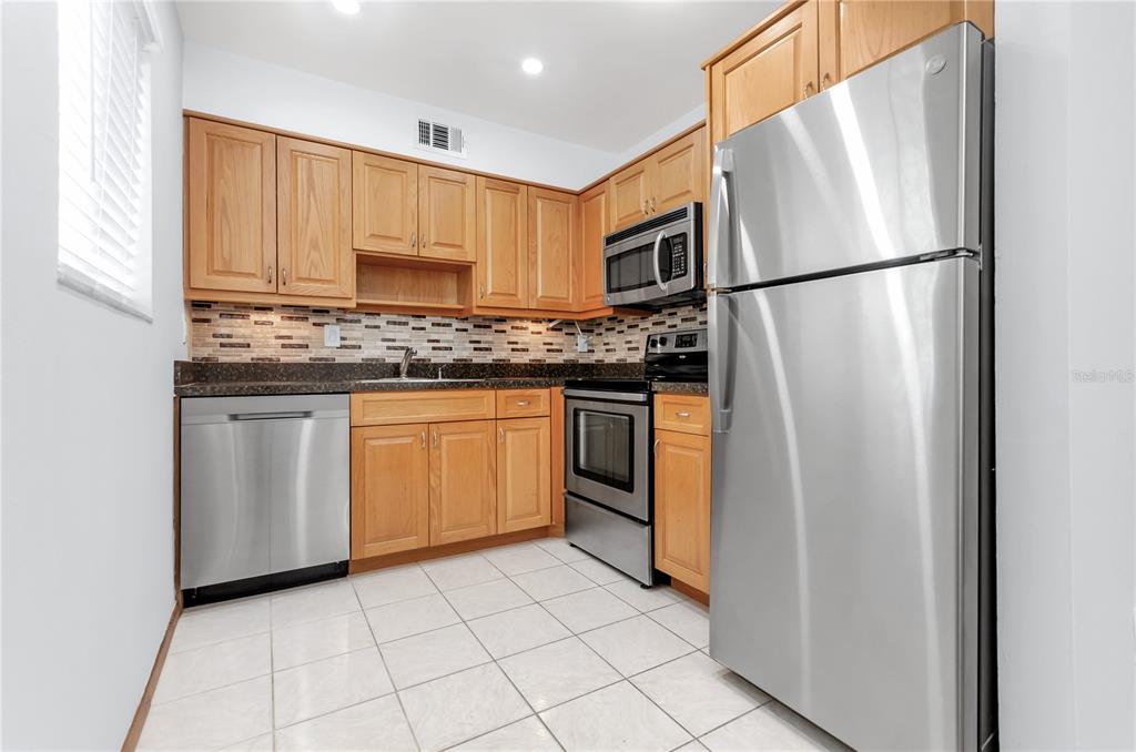 A kitchen featuring light wood cabinets, stainless steel appliances, dark countertops, and white tile flooring — 3300 FOX CHASE CIRCLE N UNIT 231, PALM HARBOR, FL