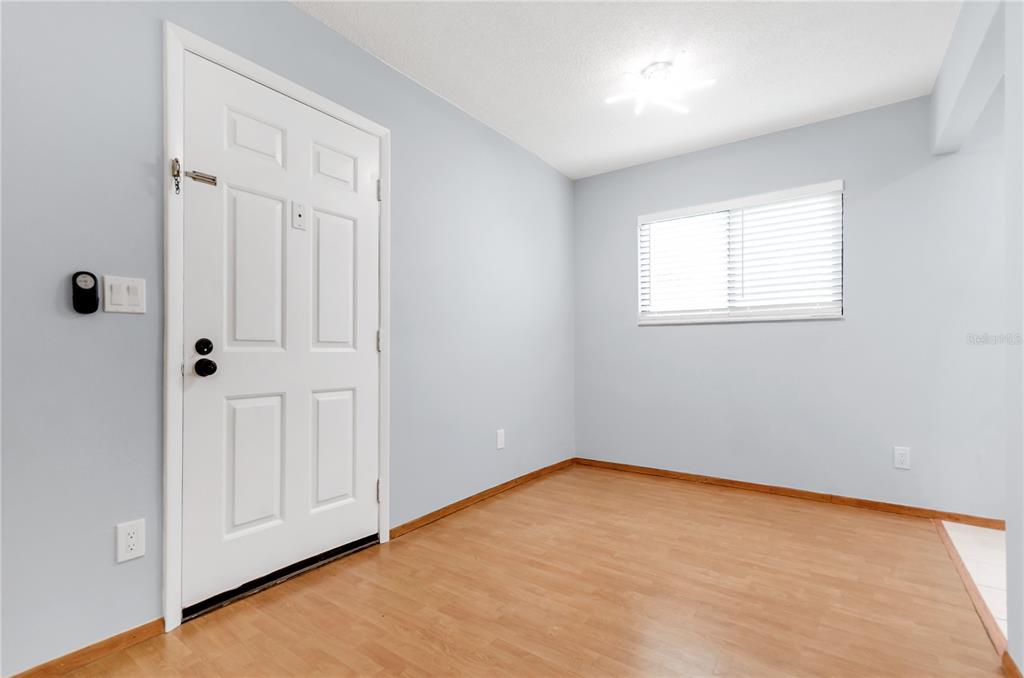 An empty room with light blue walls, wood-look flooring, a white door, and a window — 3300 FOX CHASE CIRCLE N UNIT 231, PALM HARBOR, FL