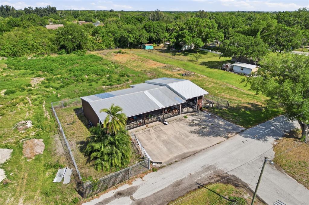 An aerial view shows a metal-roofed building with a concrete parking area and fenced yard — SHELL POINT ROAD, RUSKIN, FL