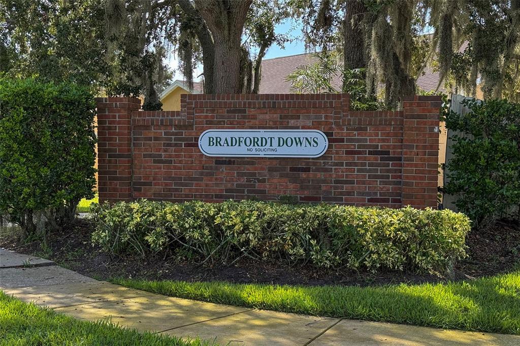 A brick entrance sign for Bradfordt Downs stands behind a manicured hedge and large trees — 12017 FAMBRIDGE, ORLANDO, FL