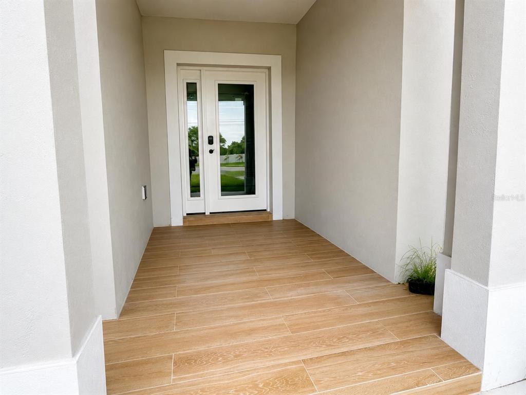 A covered entryway features wood-look tile flooring and a white front door with glass panels — 4416 MARINER BOULEVARD, SPRING HILL, FL