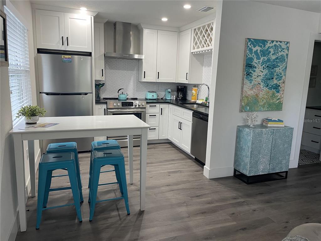A modern kitchen features white cabinets, stainless steel appliances, a tiled backsplash, and blue stools — 1910 MORRILL STREET UNIT 6, SARASOTA, FL