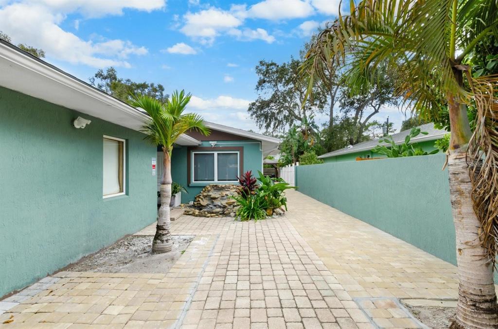 A paved courtyard features a small rock fountain, palm trees, and a green stucco exterior — 2598 WOOD STREET, SARASOTA, FL
