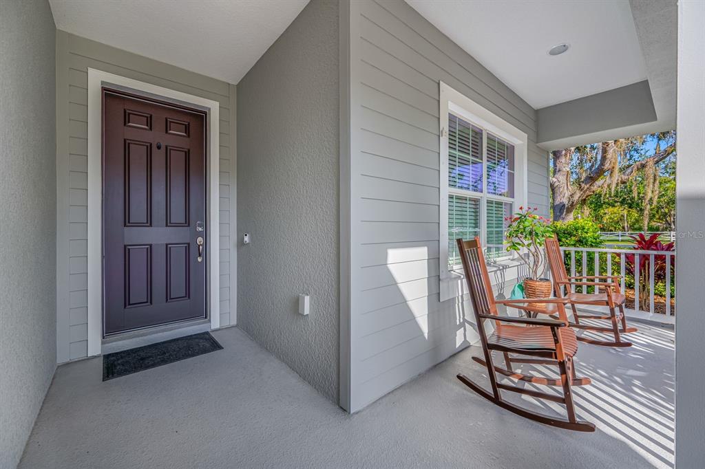 A covered front porch features a dark brown door, gray siding, and two wooden rocking chairs — 1549 WESTOVER AVENUE, PARRISH, FL