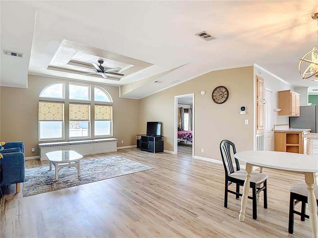 An open-concept living and dining area features light wood flooring, a tray ceiling, and windows — 452 PAR DRIVE, FROSTPROOF, FL