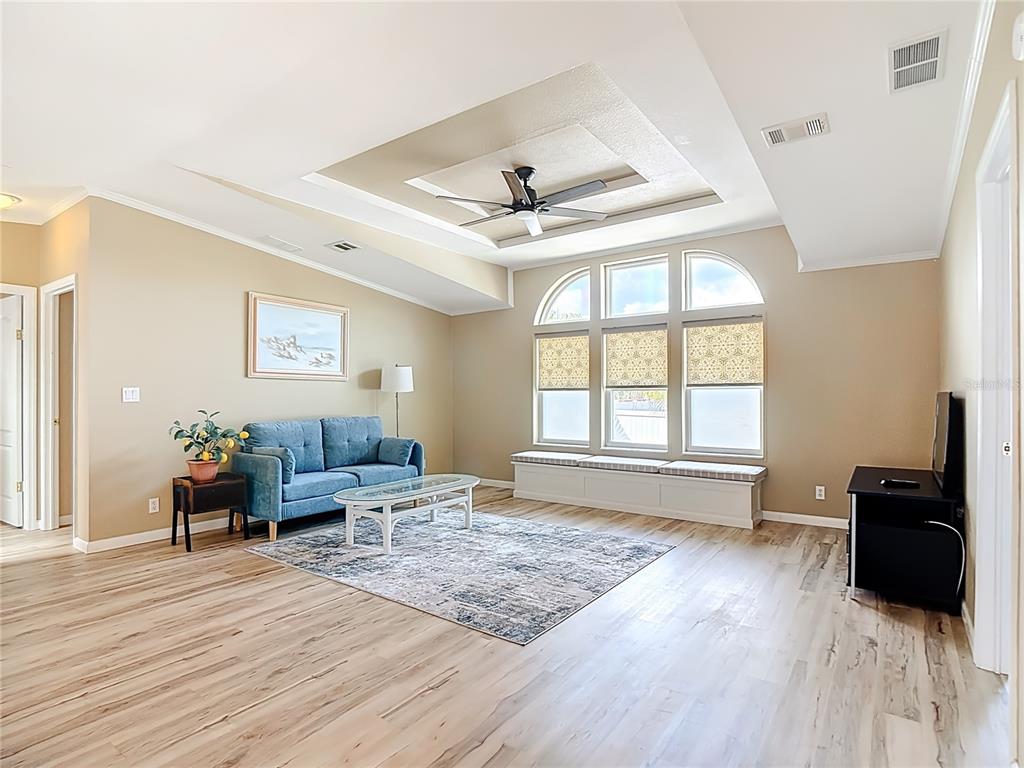 A living room with a tray ceiling, wood-look flooring, a blue sofa, and window seating — 452 PAR DRIVE, FROSTPROOF, FL