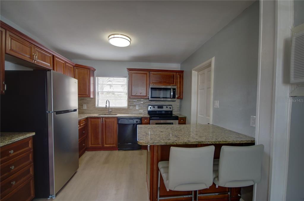 A kitchen features wood cabinets, granite countertops, stainless steel appliances, and a breakfast bar — 820 86TH AVENUE N, ST PETERSBURG, FL