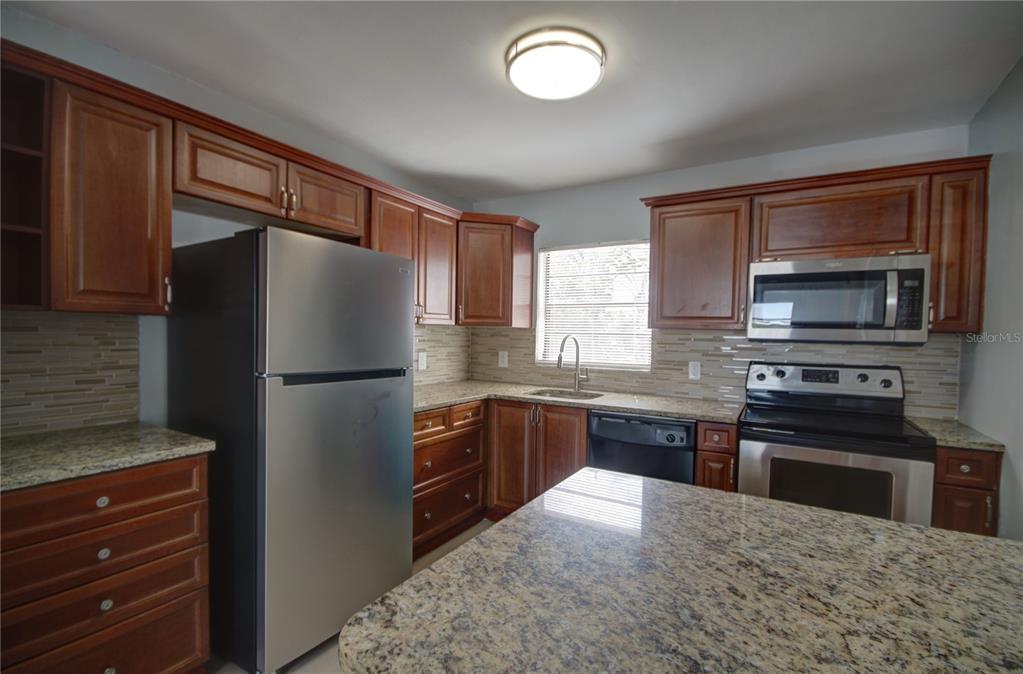 A kitchen features wood cabinets, granite countertops, stainless steel appliances, and a tiled backsplash — 820 86TH AVENUE N, ST PETERSBURG, FL