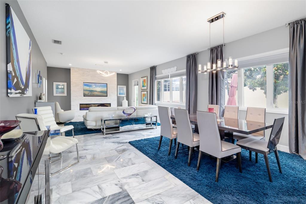 A modern open-concept living and dining area features marble floors, blue rugs, and a fireplace — 5237 97TH STREET E, BRADENTON, FL