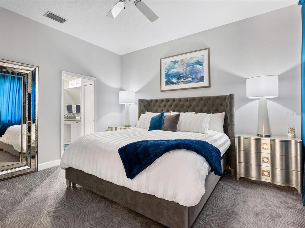 A bedroom features a tufted gray headboard, white bedding with a blue throw, and mirrored furniture — 5237 97TH STREET E, BRADENTON, FL