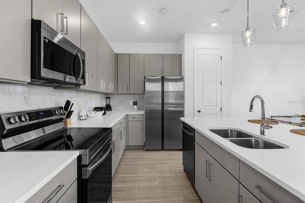 A modern kitchen features gray cabinetry, stainless steel appliances, white countertops, and a central island — 935 CONCH ROAD, DAVENPORT, FL
