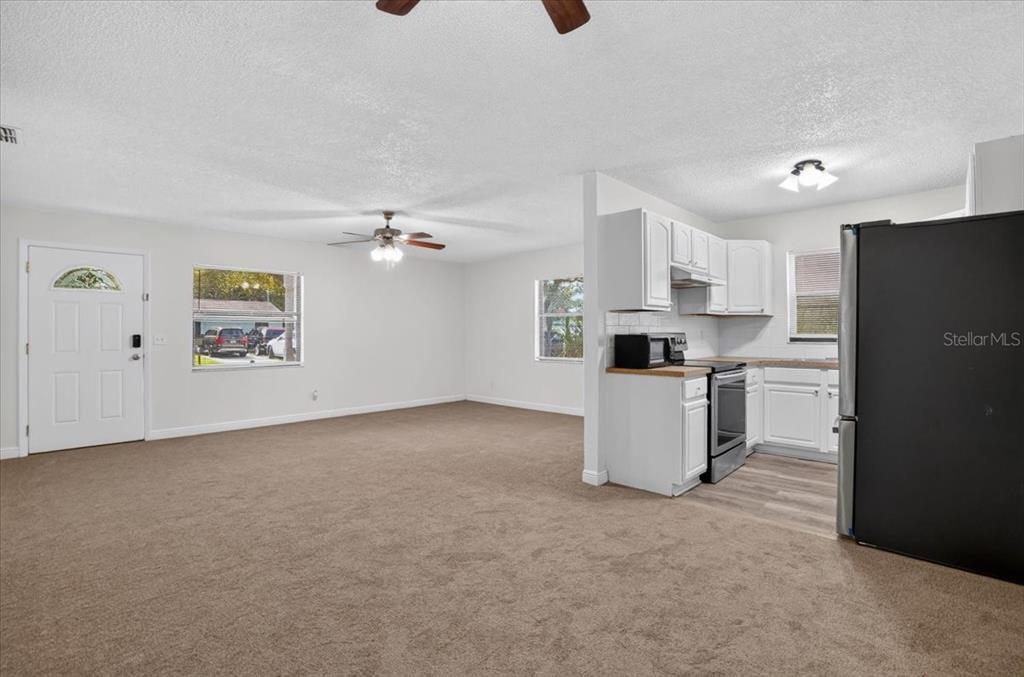 An open-concept living room with beige carpeting connects to a kitchen featuring white cabinets — 12641 116TH LANE, SEMINOLE, FL