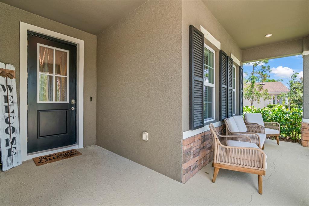 A covered front porch features a black door, two wicker chairs, and stone siding accents — 2443 PORTICO STREET, ODESSA, FL
