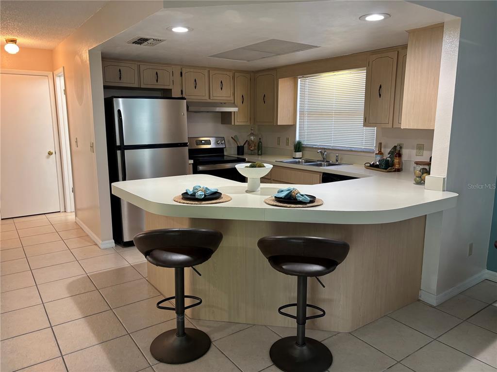 A kitchen features light wood cabinets, a stainless steel refrigerator, and a curved peninsula countertop — 7619 VIENNA LANE, PORT RICHEY, FL