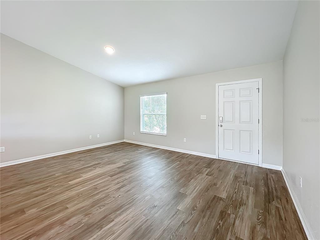 An empty room features light-colored walls, wood-look flooring, a single window, and a white door — 178 PINE COURSE, OCALA, FL