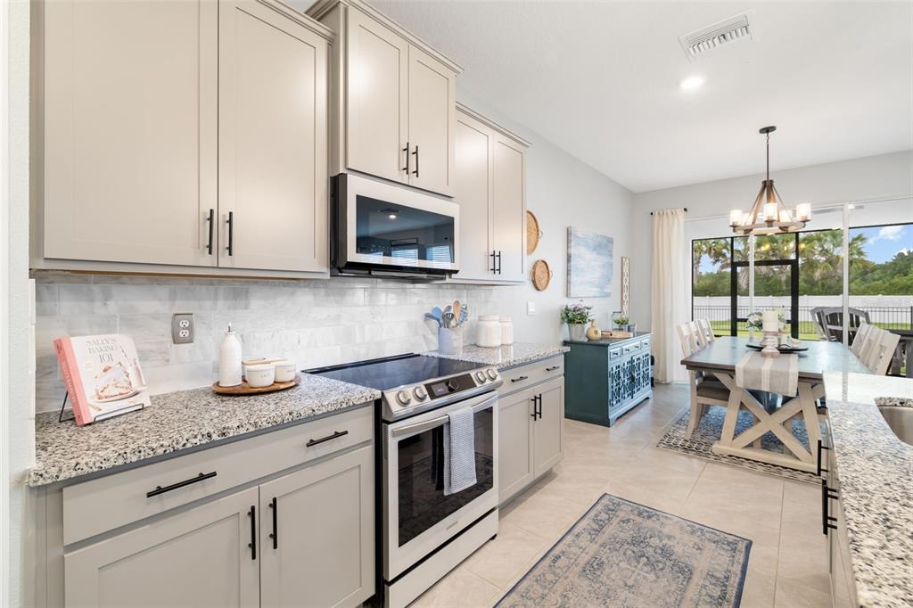 A kitchen with light gray cabinets, granite countertops, and a dining area with a chandelier — 15905 5TH AVENUE E, BRADENTON, FL
