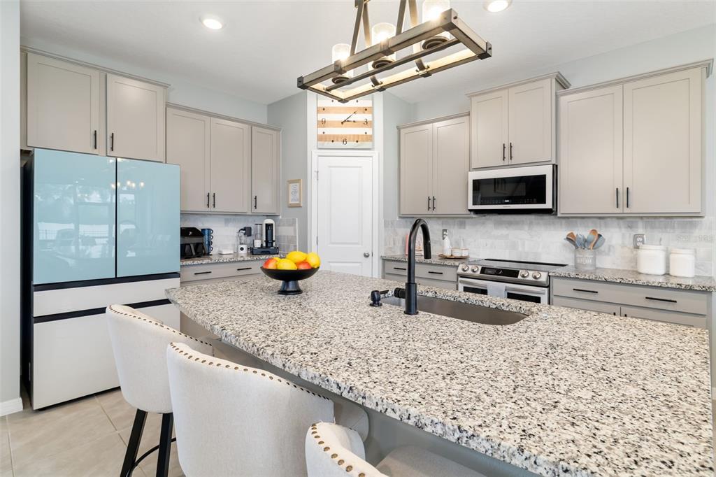 A kitchen features light gray cabinets, granite countertops, a central island, and a blue refrigerator — 15905 5TH AVENUE E, BRADENTON, FL