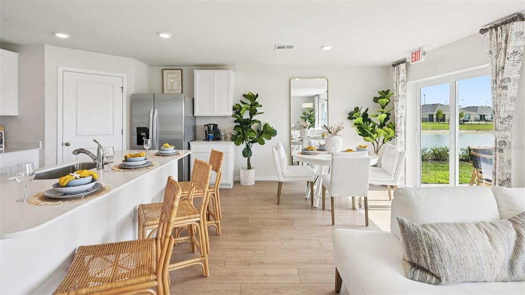 A bright open-concept kitchen and dining area features white cabinetry, rattan stools, and lake views — 1551 POWELL VALLEY DRIVE, PORT CHARLOTTE, FL