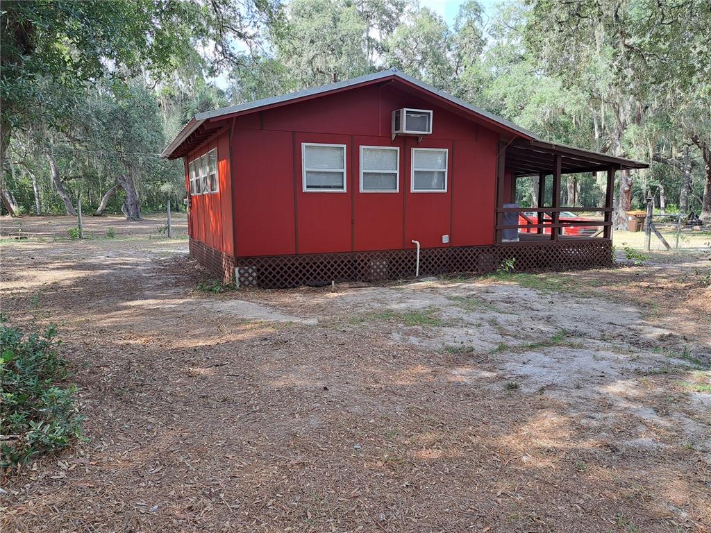 A red, single-story house with a porch and lattice skirting sits on a wooded lot — 17010 SE 95TH ST RD, OCKLAWAHA, FL