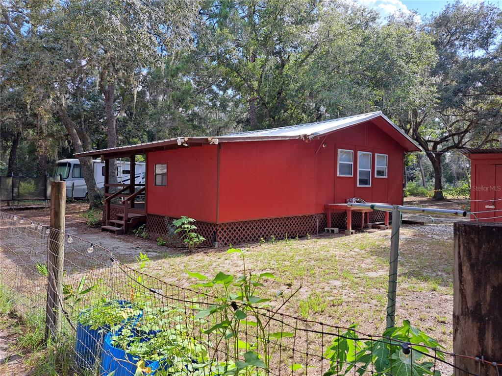 A red, single-story house with a metal roof sits on a lot with trees — 17010 SE 95TH ST RD, OCKLAWAHA, FL