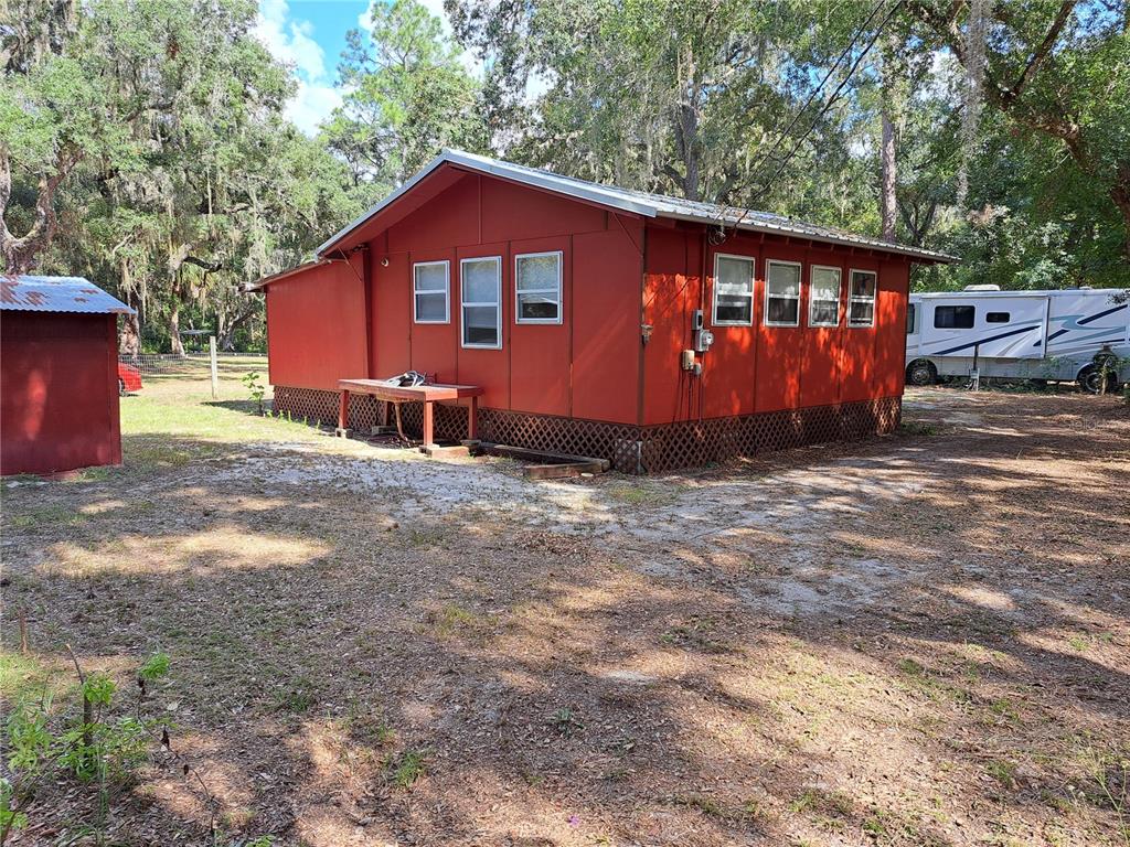 A red exterior house with a metal roof stands on a dirt lot with trees — 17010 SE 95TH ST RD, OCKLAWAHA, FL