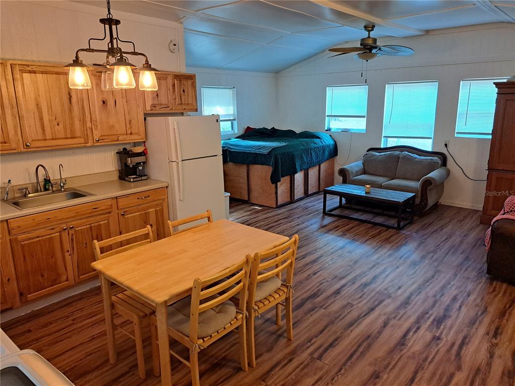 An open-concept kitchen and living area features wood-look flooring, light wood cabinets, and a bed — 17010 SE 95TH ST RD, OCKLAWAHA, FL