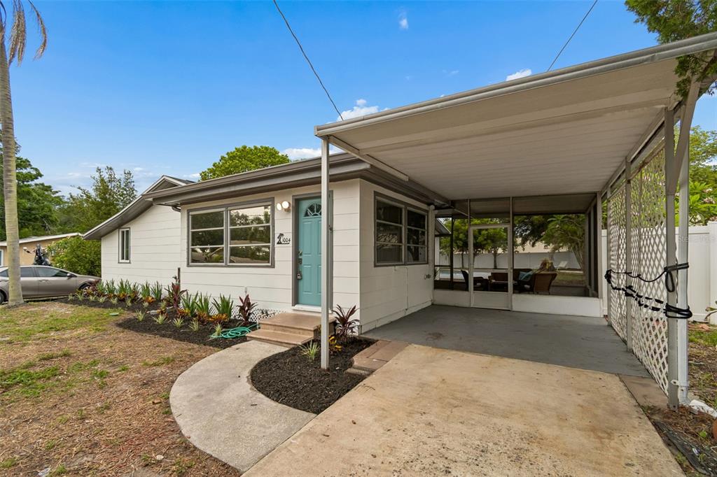 A single-story house with a teal front door, a carport, and a landscaped front yard — 1004 WASHINGTON AVENUE, LARGO, FL