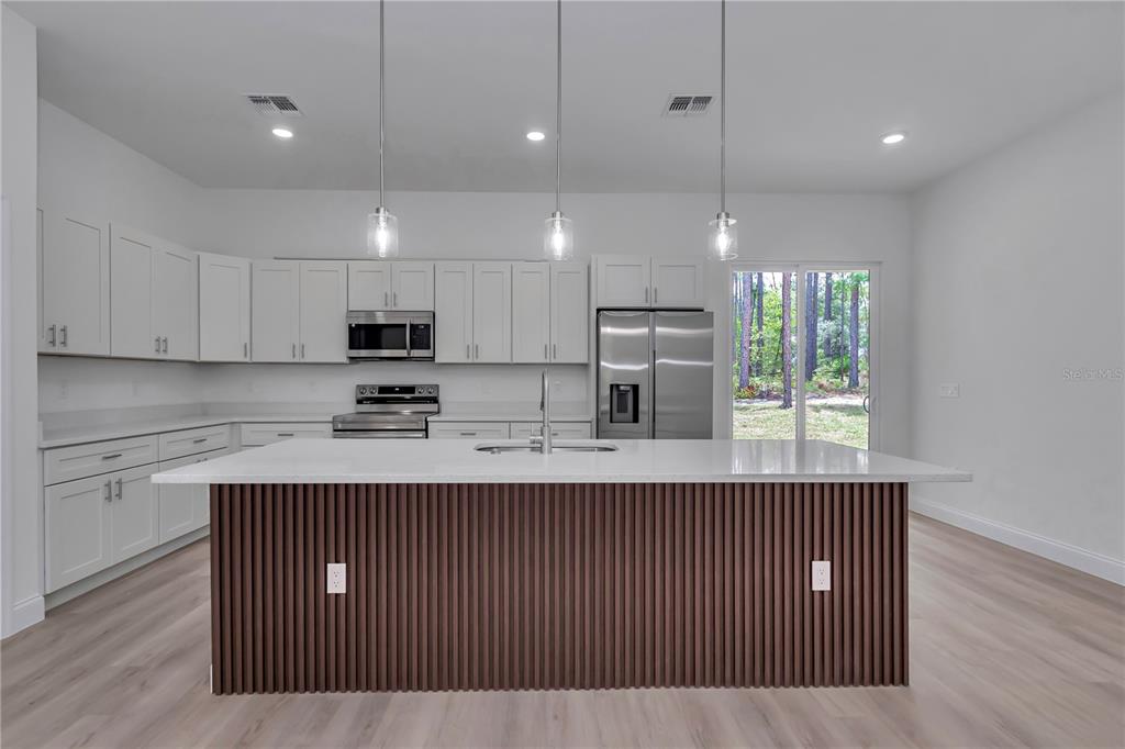 A modern kitchen features white cabinetry, stainless steel appliances, and a slatted wood kitchen island — 7565 N SANTOS DRIVE, CITRUS SPRINGS, FL