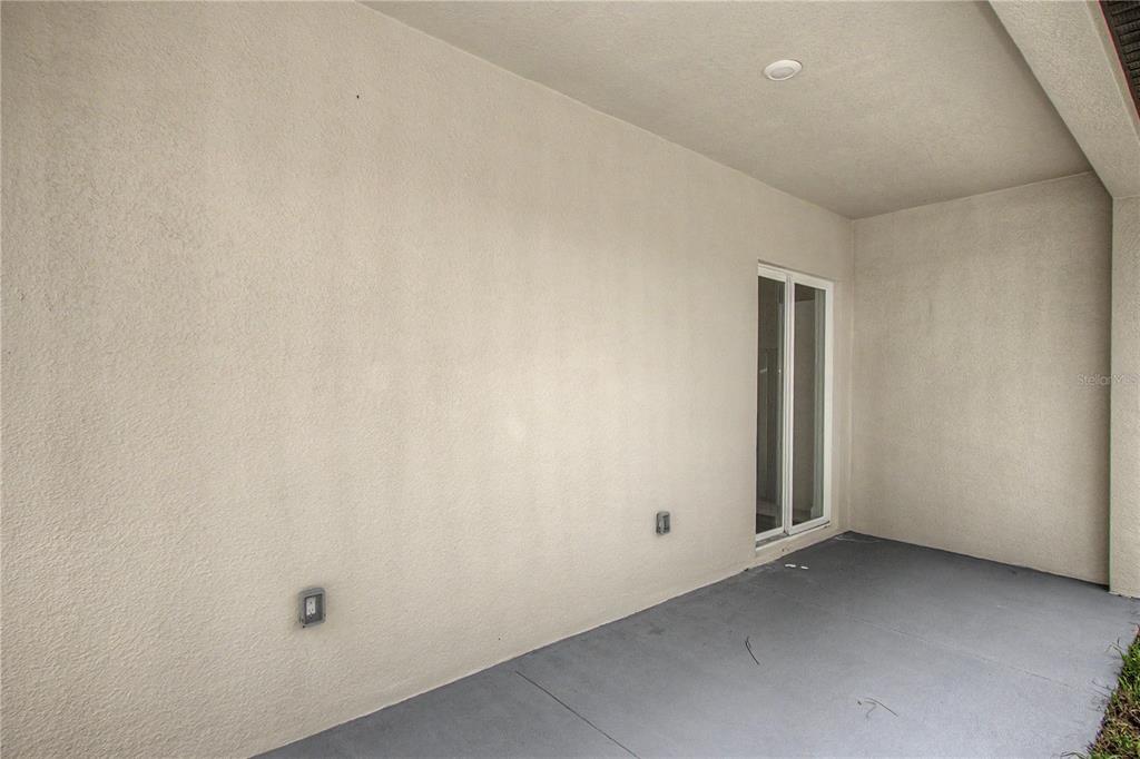A covered concrete patio features beige stucco walls and a sliding glass door — 7565 N SANTOS DRIVE, CITRUS SPRINGS, FL