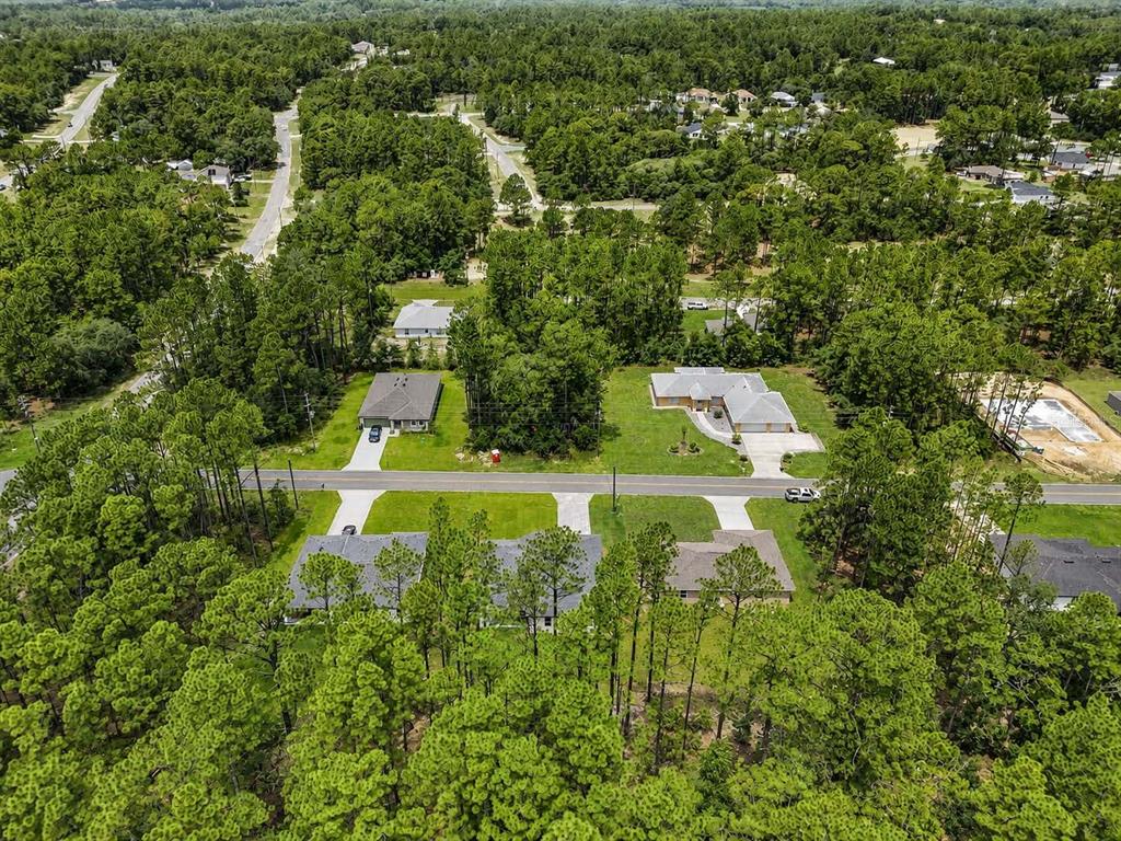 An aerial view shows several houses surrounded by dense forest and a paved road — 7565 N SANTOS DRIVE, CITRUS SPRINGS, FL