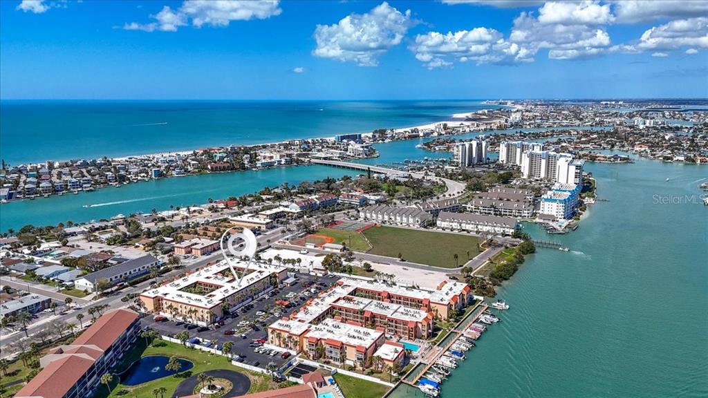 An aerial view shows a multi-story residential complex near a waterway and coastal beach — 8911 BLIND PASS ROAD UNIT 118, ST PETE BEACH, FL