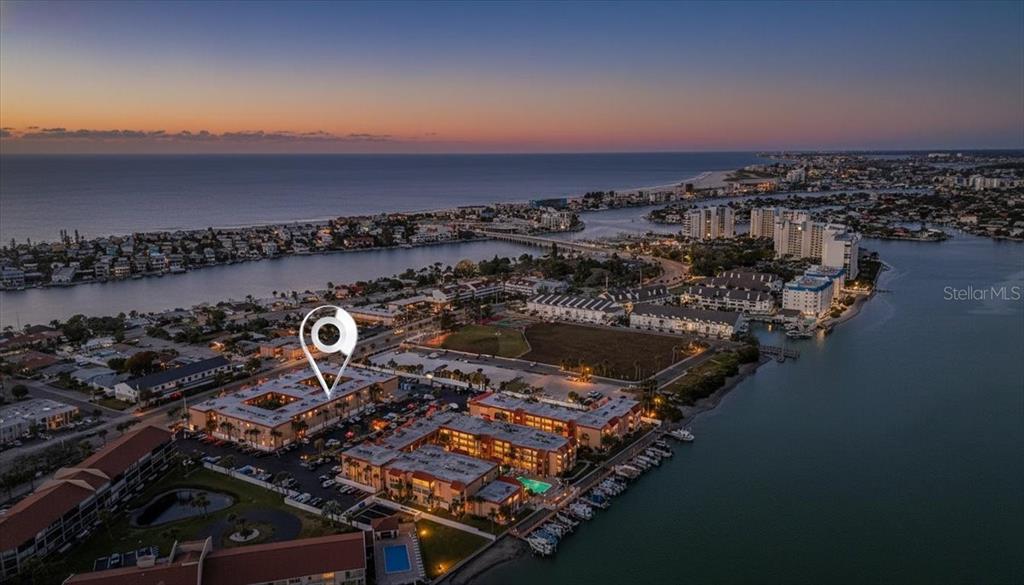 An aerial view shows a waterfront apartment complex at sunset with a location pin marker — 8911 BLIND PASS ROAD UNIT 118, ST PETE BEACH, FL
