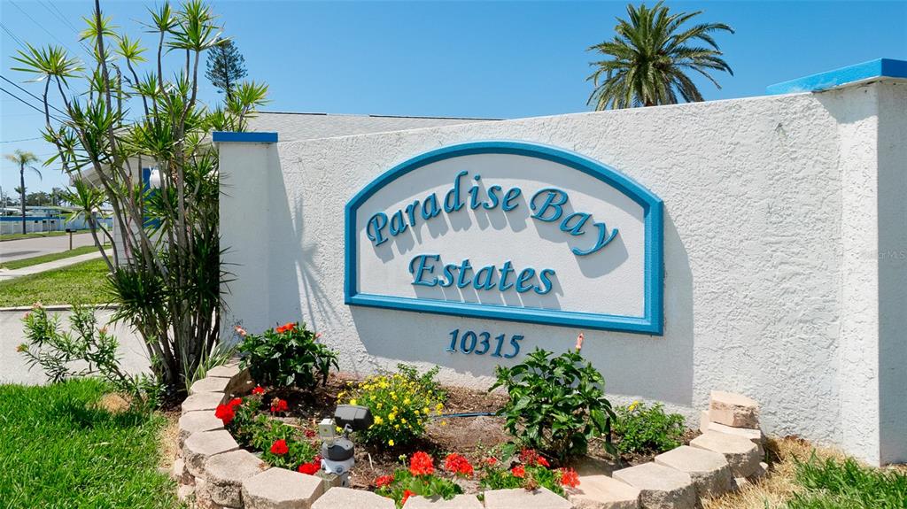 A white stucco sign for Paradise Bay Estates sits behind a small landscaped garden bed — 10315 CORTEZ ROAD W UNIT 1-4, BRADENTON, FL