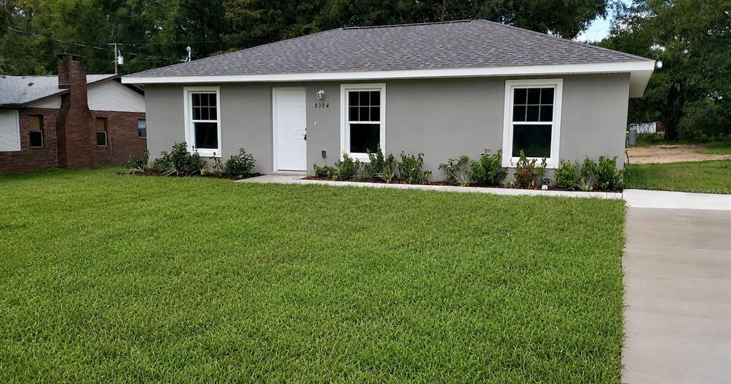 A gray, single-story house with a white door and windows sits behind a green lawn — 13750 SW 103RD PLACE, DUNNELLON, FL
