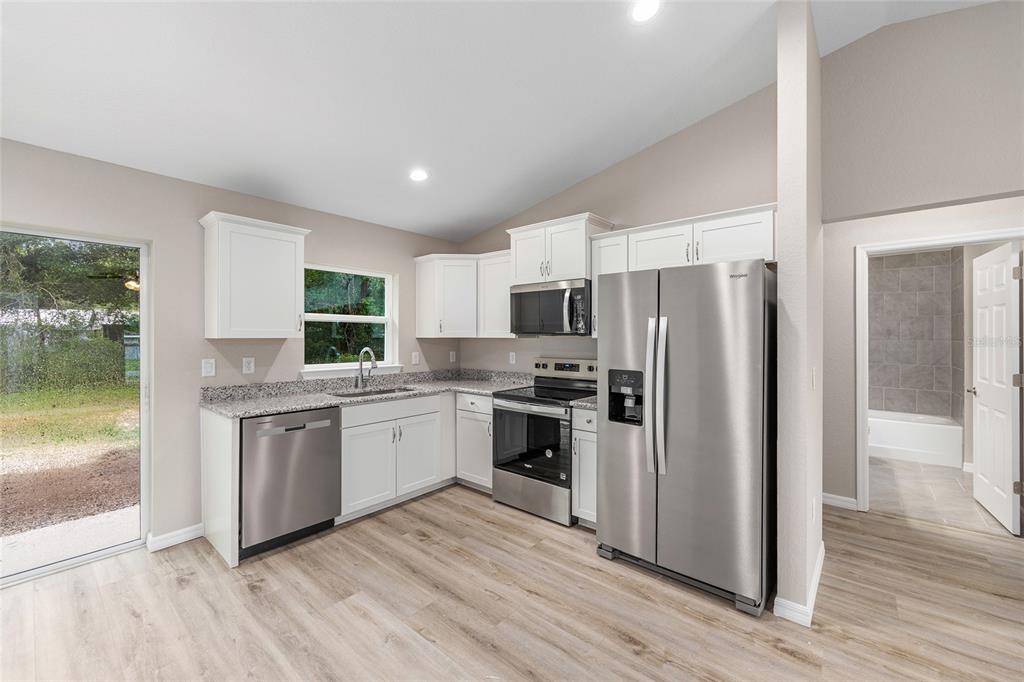 A kitchen with white cabinets, granite countertops, stainless steel appliances, and light wood-look flooring — 13750 SW 103RD PLACE, DUNNELLON, FL