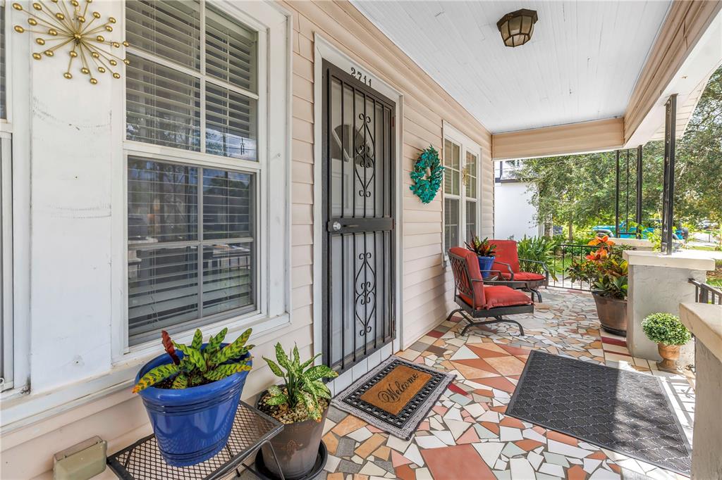 A covered front porch features a mosaic tile floor, two red chairs, and potted plants — 2711 W FIG STREET, TAMPA, FL
