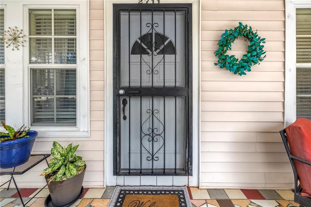 A front porch features a security screen door, a wreath, potted plants, and tiled flooring — 2711 W FIG STREET, TAMPA, FL