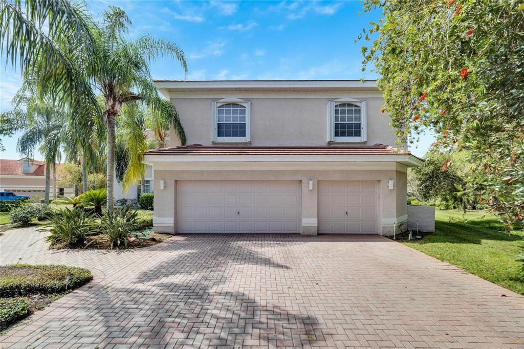 A two-story house with a beige stucco exterior, a brick driveway, and a three-car garage — 17904 CACHET ISLE DRIVE, TAMPA, FL