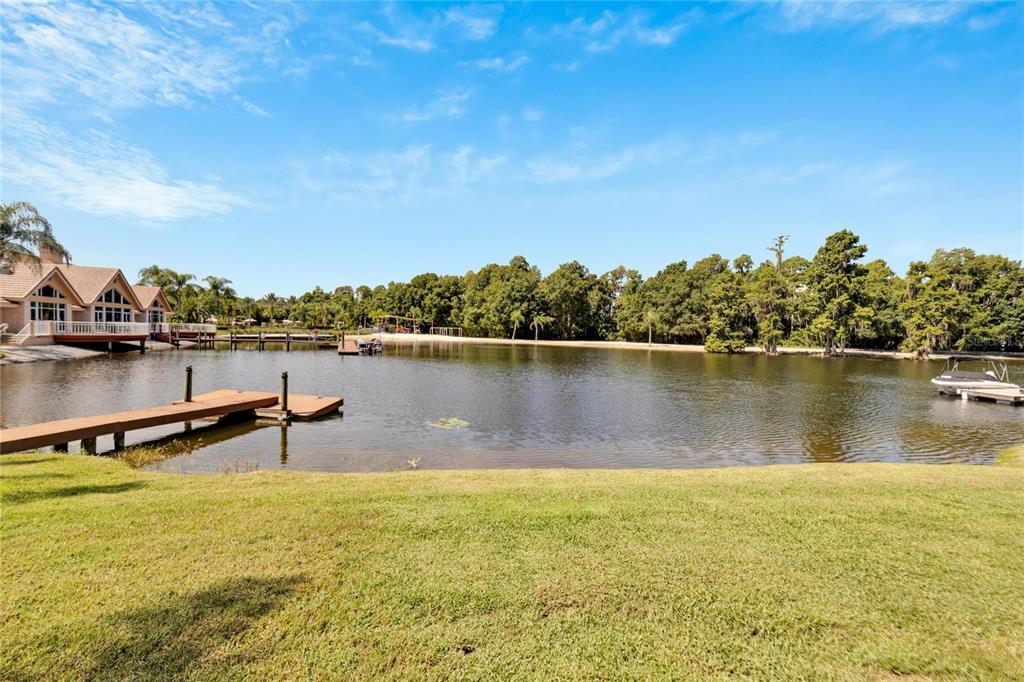 A grassy lawn leads to a lake with a wooden dock and a house nearby — 17904 CACHET ISLE DRIVE, TAMPA, FL