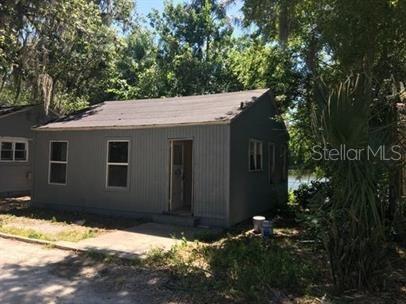 A small, gray, single-story house with a gabled roof sits among trees near a lake — 4 LUCERNE CIRCLE, LEESBURG, FL