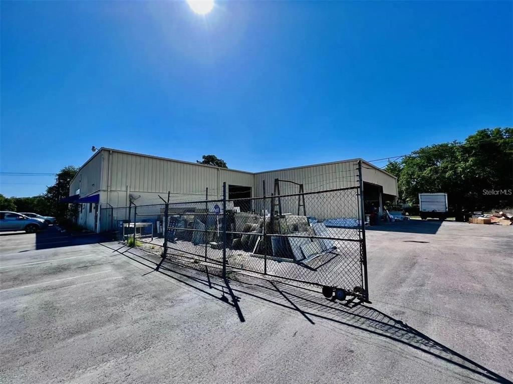 A fenced-in outdoor storage area sits beside a large, light-colored industrial warehouse building — 2398 63RD AVENUE E, BRADENTON, FL