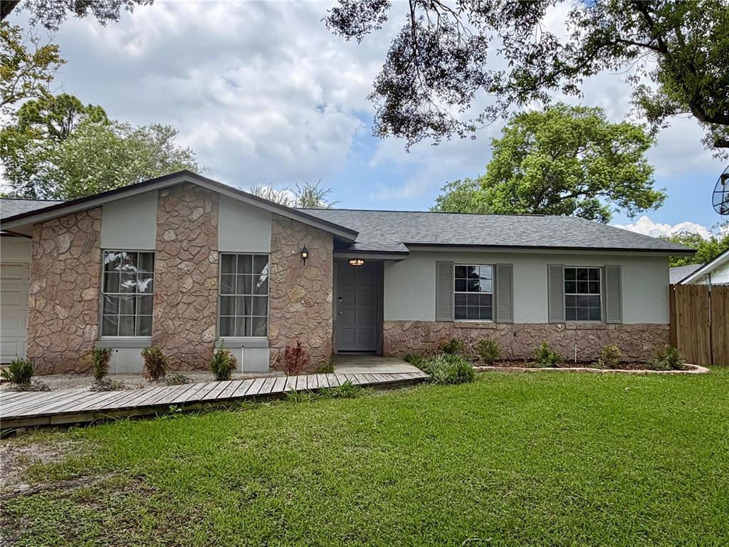 A single-story house features a stone facade, gray siding, and a wooden ramp leading to the entrance — 1 KING ARTHUR COURT, CASSELBERRY, FL
