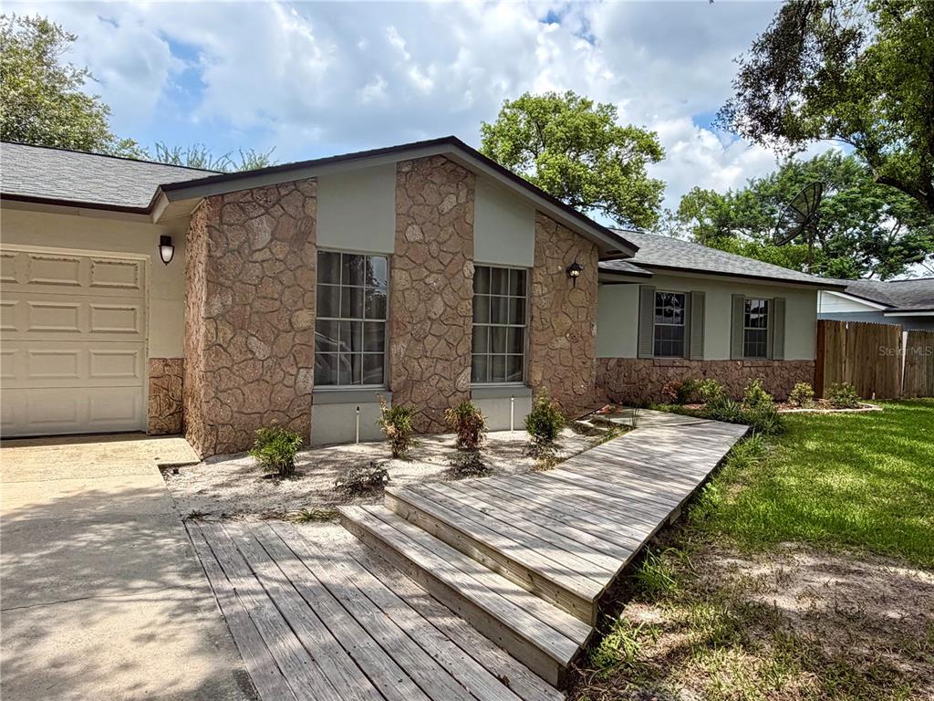 A single-story house features a stone facade, a wooden walkway, and a concrete driveway — 1 KING ARTHUR COURT, CASSELBERRY, FL
