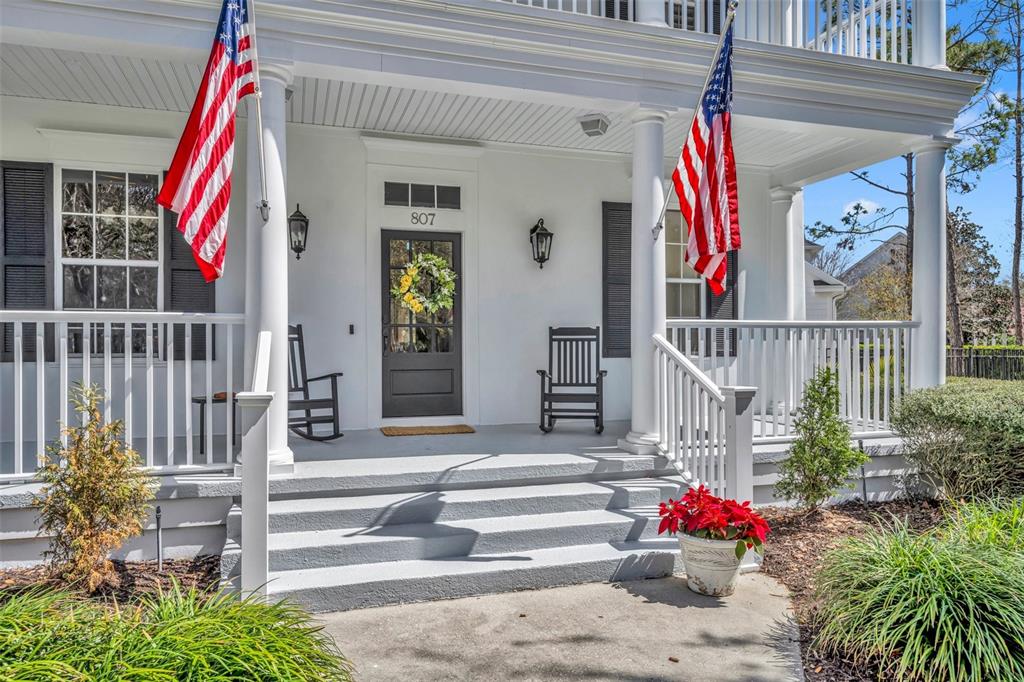 A white house exterior features a front porch with two American flags and rocking chairs — 807 OAK SHADOWS ROAD, CELEBRATION, FL