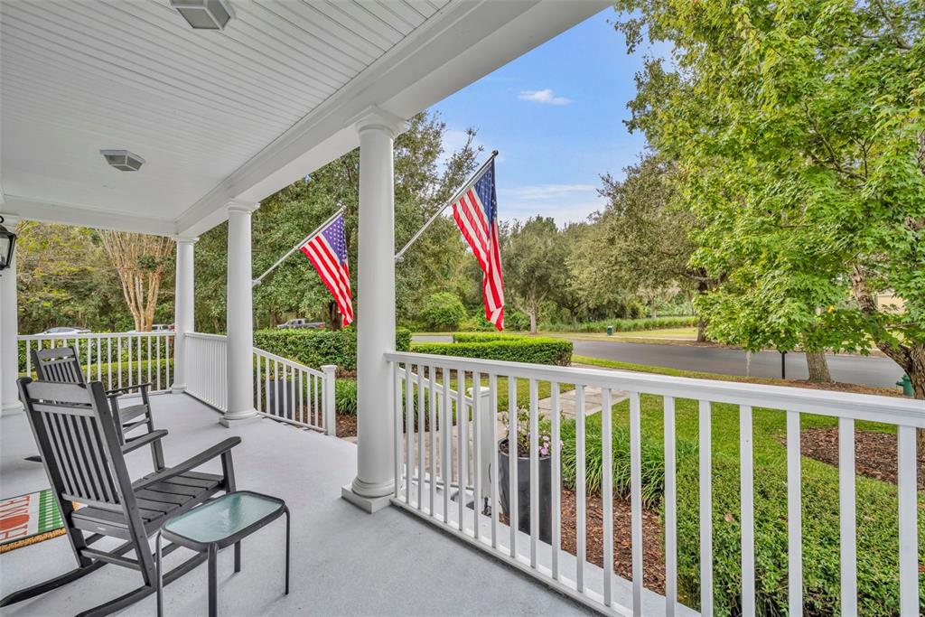 A covered front porch features white railings, columns, rocking chairs, and two American flags — 807 OAK SHADOWS ROAD, CELEBRATION, FL