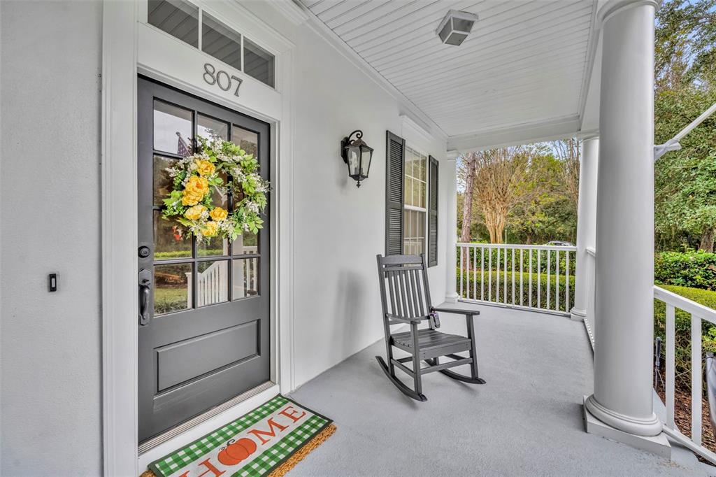 A covered front porch features a dark gray door, a rocking chair, and white columns — 807 OAK SHADOWS ROAD, CELEBRATION, FL